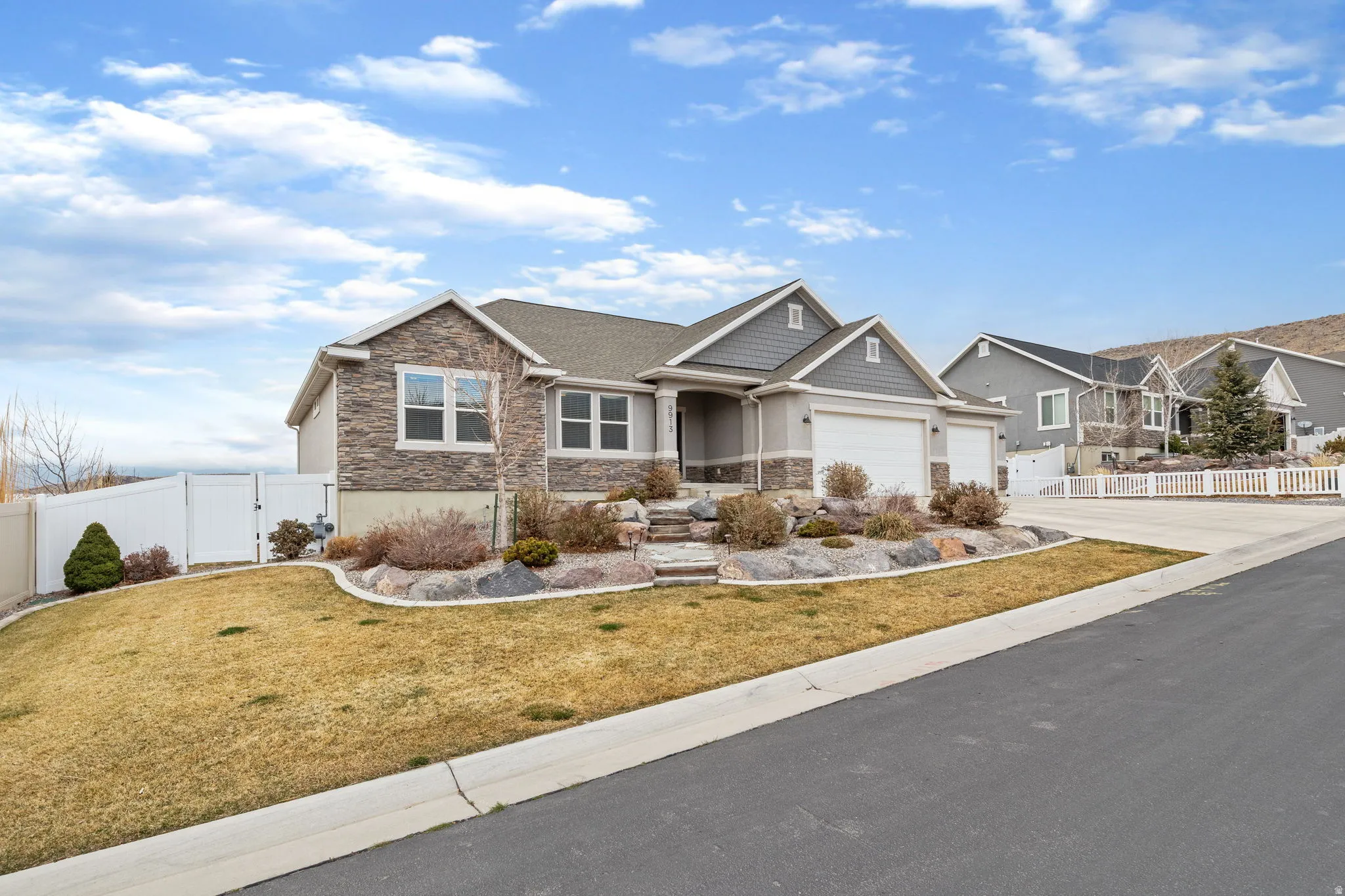 Craftsman-style house with stone siding, a gate, driveway, and a garage