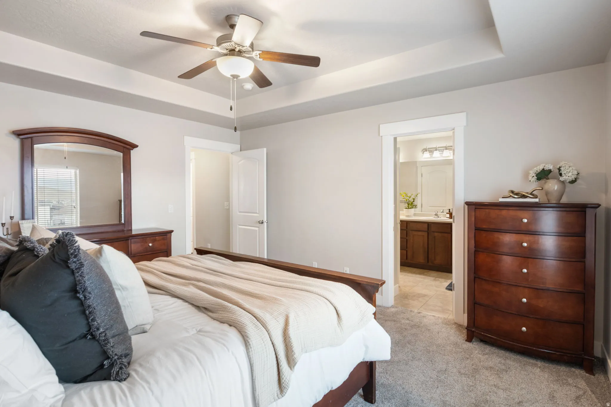 Carpeted bedroom with a raised ceiling, a ceiling fan, and connected bathroom