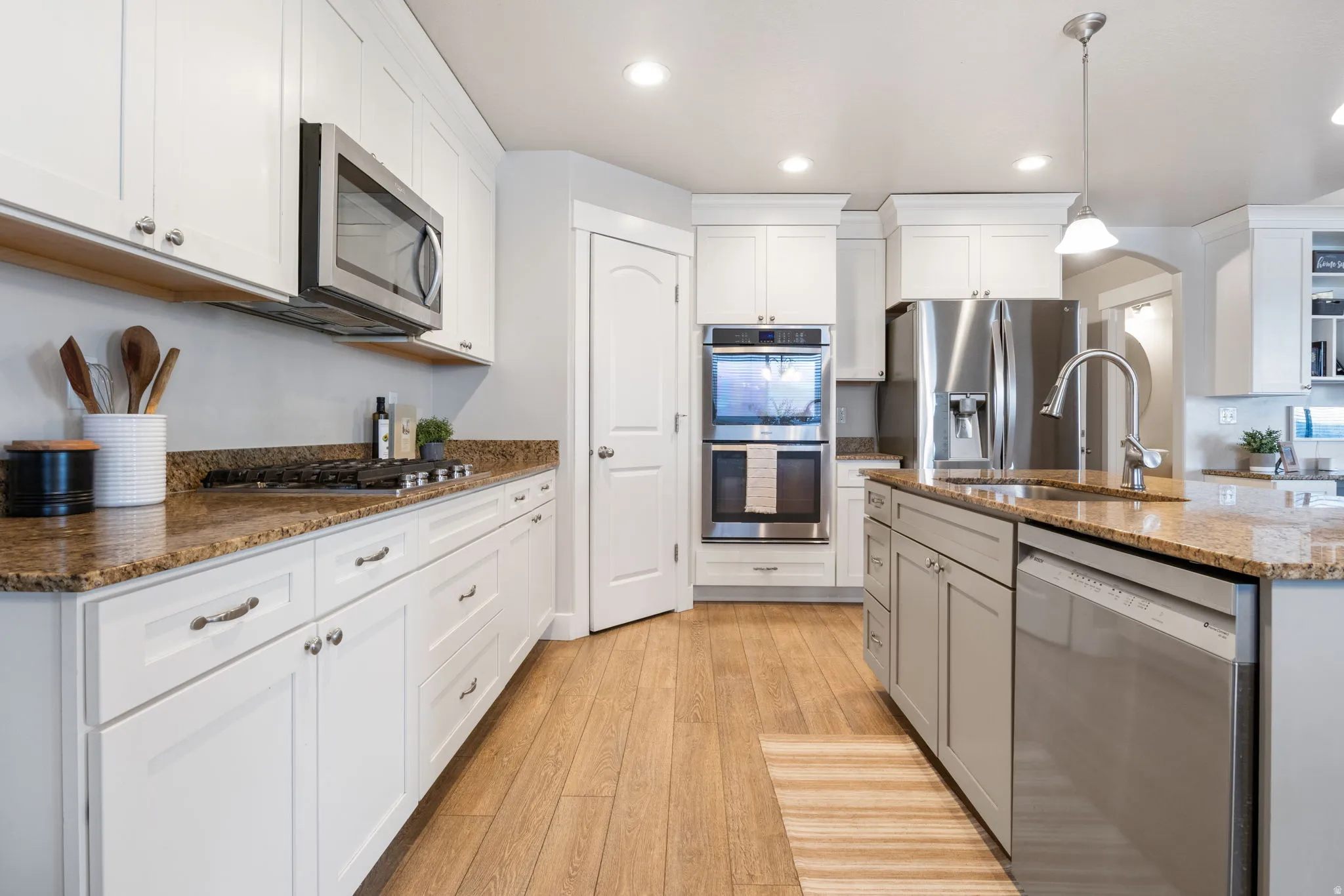 Kitchen featuring dark stone counters, stainless steel appliances, light wood-style floors, and white cabinetry