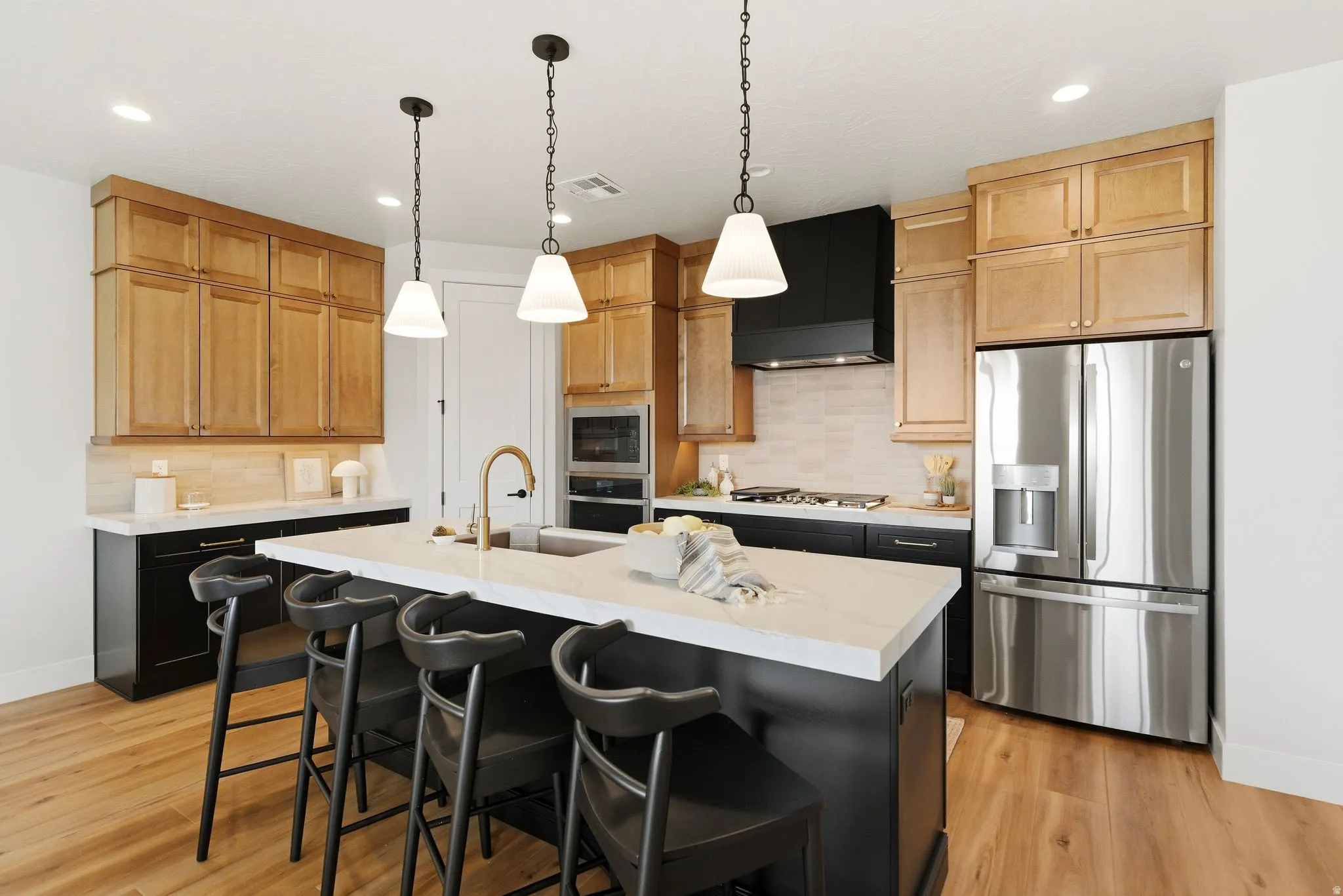 Kitchen with stainless steel appliances, a kitchen breakfast bar, an island with sink, pendant lighting, and light wood finished floors
