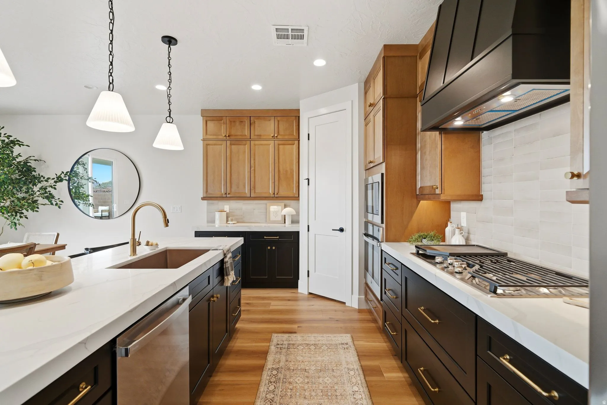 Kitchen featuring light stone countertops, stainless steel appliances, light wood-style floors, decorative light fixtures, and dual tone cabinets