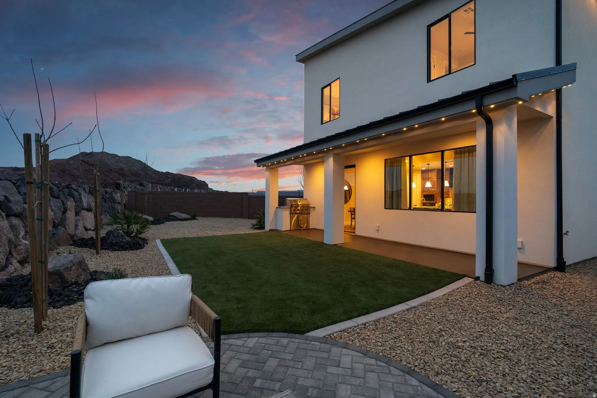 Back of house at dusk featuring a patio, stucco siding, an outdoor kitchen, a fenced backyard, and a mountain view