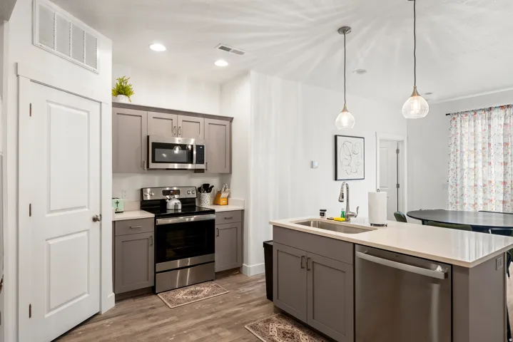 Modern kitchen featuring stainless steel appliances, a spacious island with white quartz countertop and waterfall edge, dual pendant lighting, wood-finish flooring, and ample cabinetry with hardware accents throughout