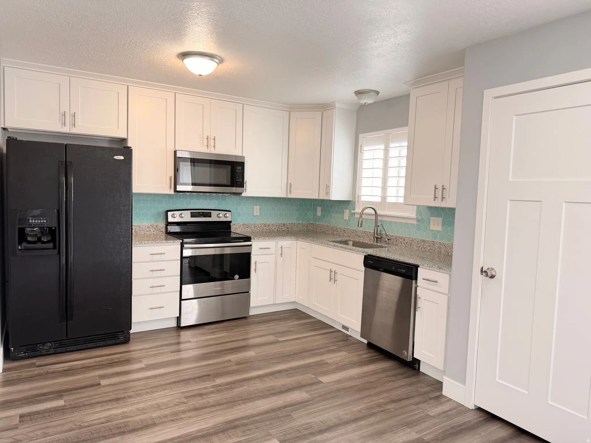 Kitchen featuring stainless steel appliances, white cabinets, a textured ceiling, light stone counters, and dark wood-style floors