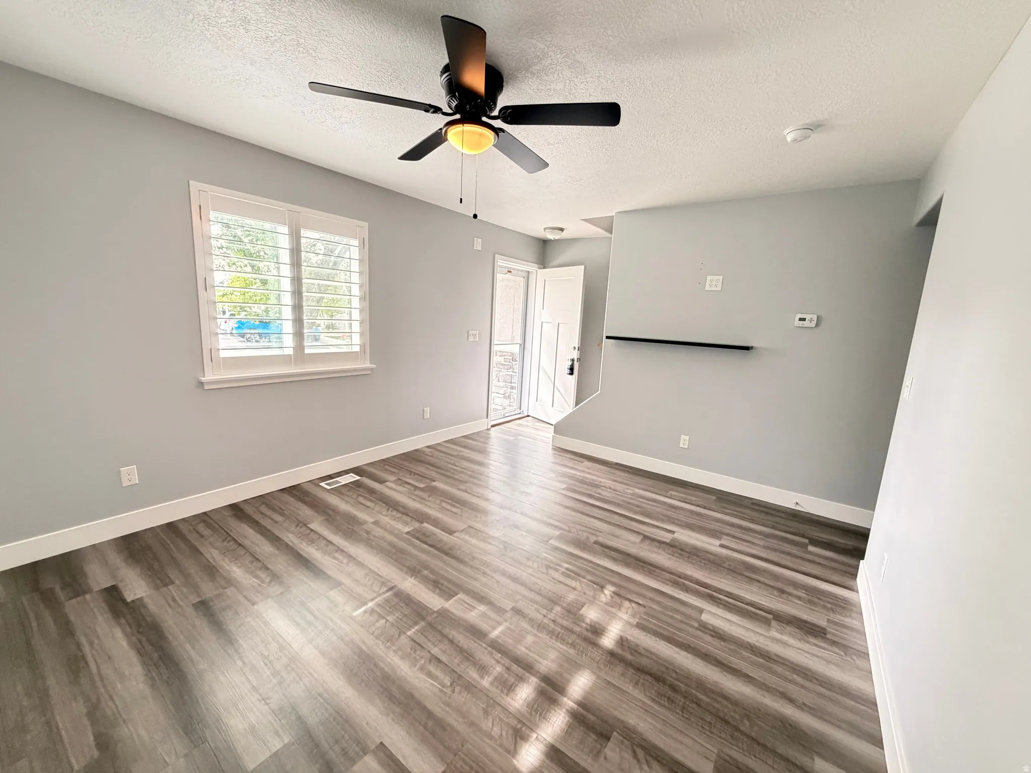 Unfurnished living room with ceiling fan, dark wood finished floors, and a textured ceiling