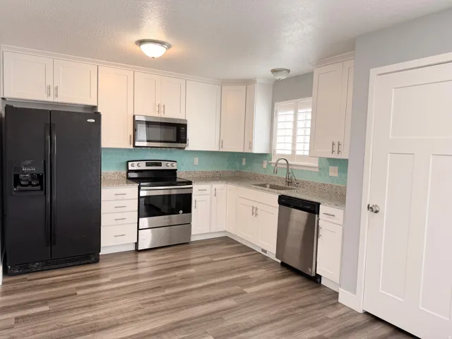 Kitchen featuring stainless steel appliances, white cabinets, a textured ceiling, light stone counters, and dark wood-style floors