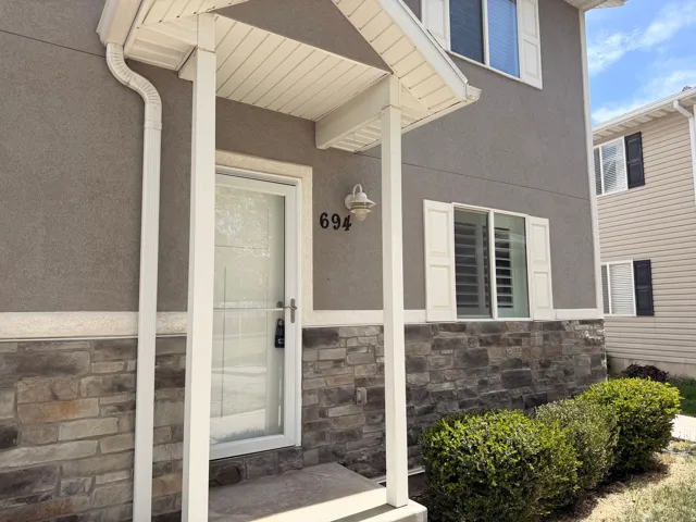 Entrance to property featuring stone siding, stucco siding, and a porch