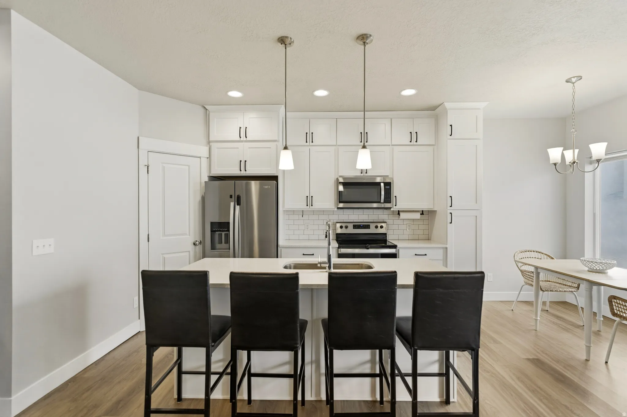 Kitchen featuring stainless steel appliances, an island with sink, white cabinets, and solid surface counters