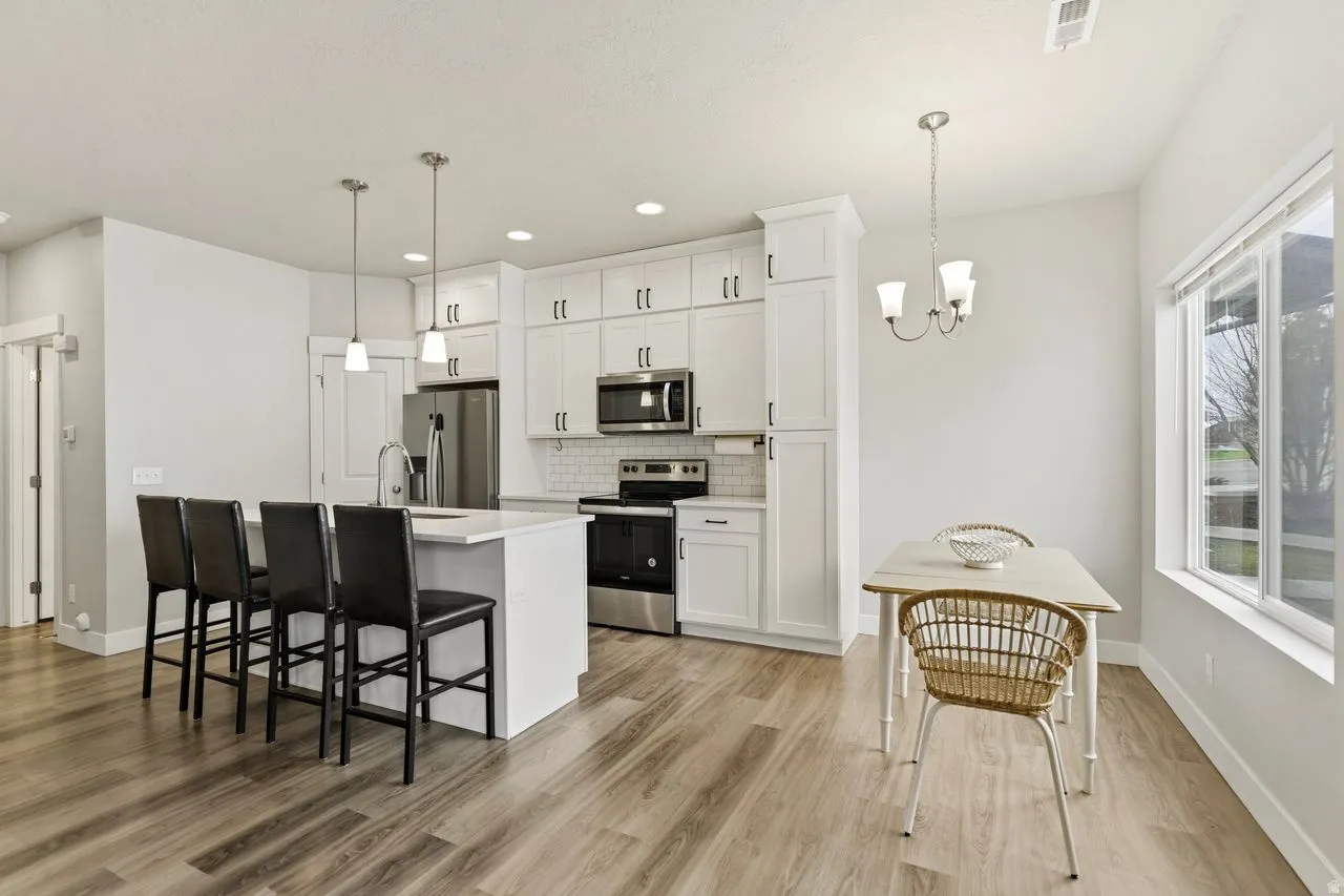 Kitchen with stainless steel appliances, a breakfast bar area, white cabinetry, light wood finished floors, and tasteful backsplash