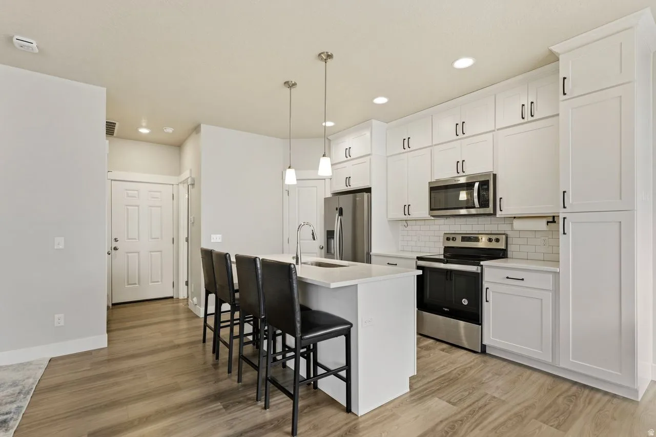Kitchen with stainless steel appliances, white cabinetry, a kitchen bar, hanging light fixtures, and a center island with sink