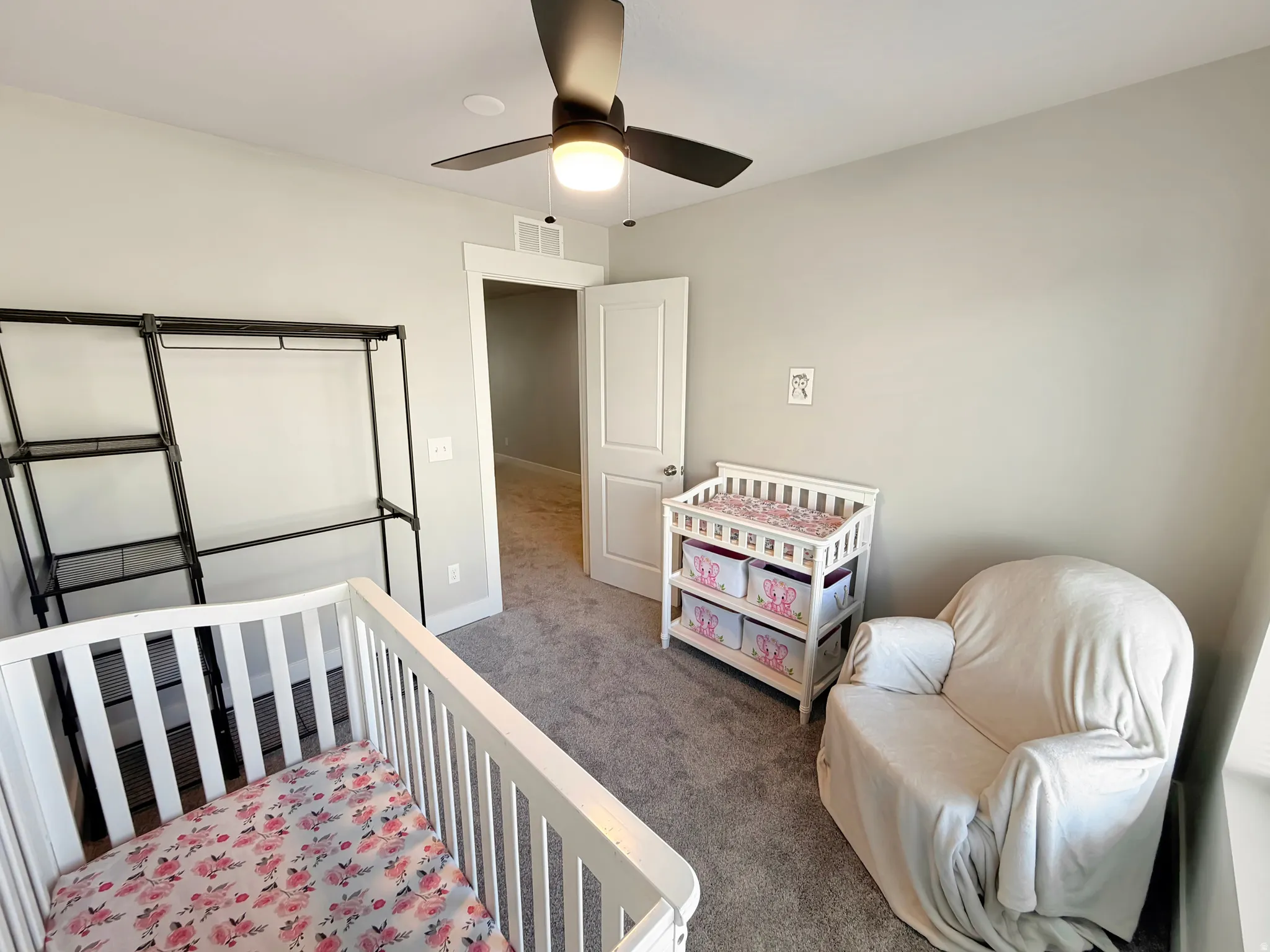 Carpeted bedroom featuring a crib and a ceiling fan