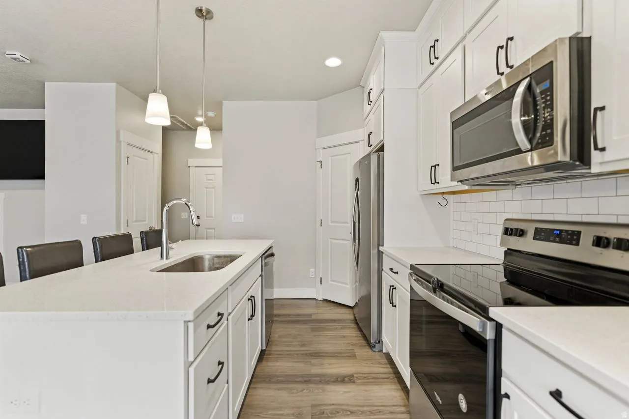 Kitchen featuring stainless steel appliances, an island with sink, white cabinets, and light solid surface counters