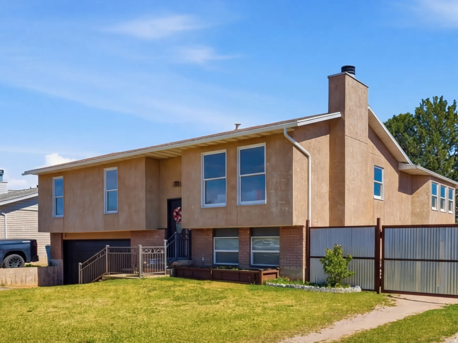 View of front of house featuring driveway, stucco siding, a chimney, an attached garage, and a gate