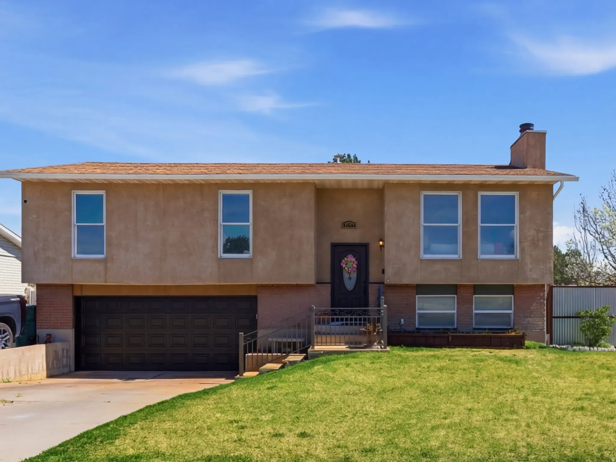 Split foyer home featuring a garage, concrete driveway, a chimney, and stucco siding