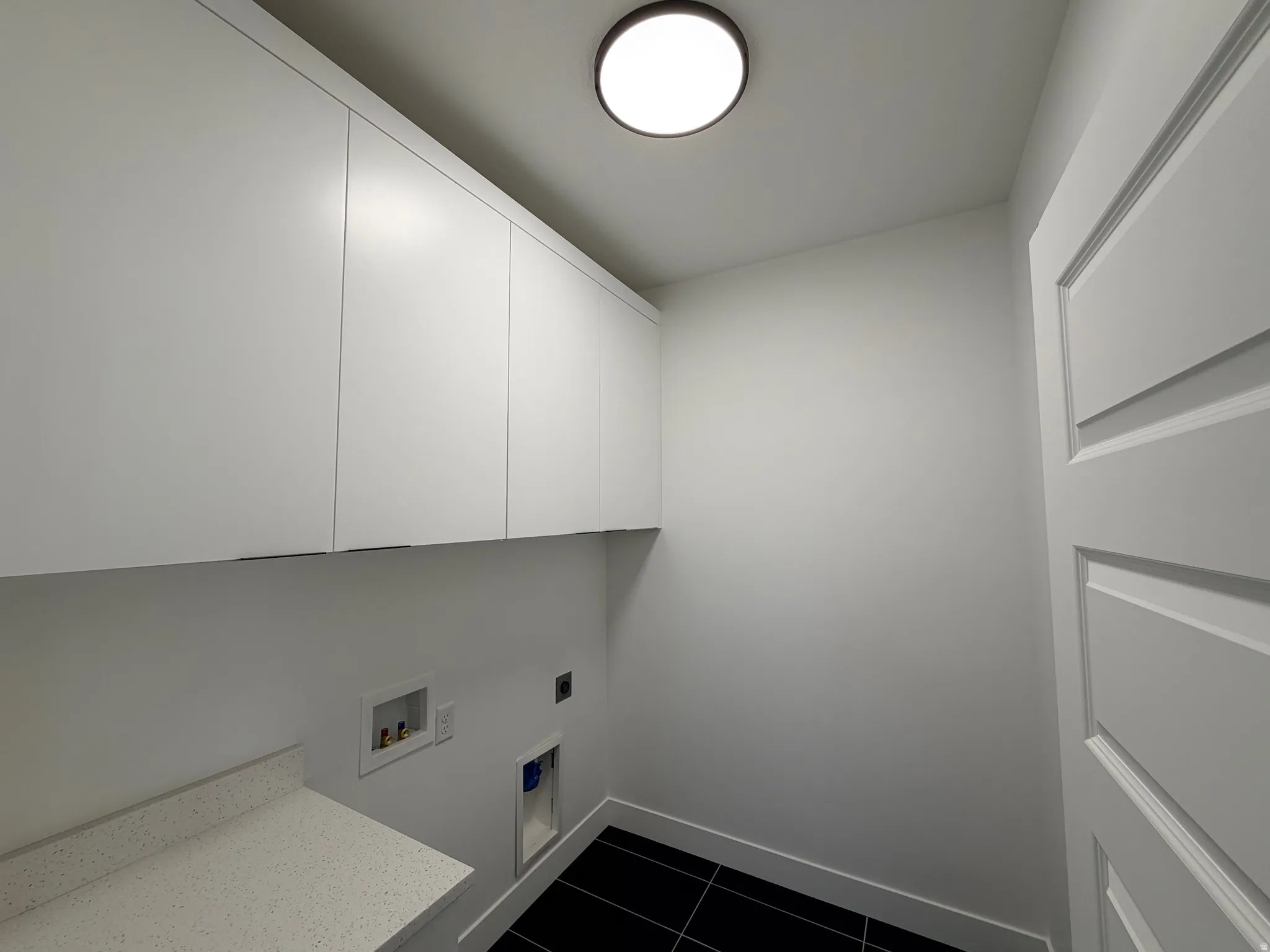 Laundry area with dark tile patterned floors, hookup for an electric dryer, cabinet space, and hookup for a washing machine