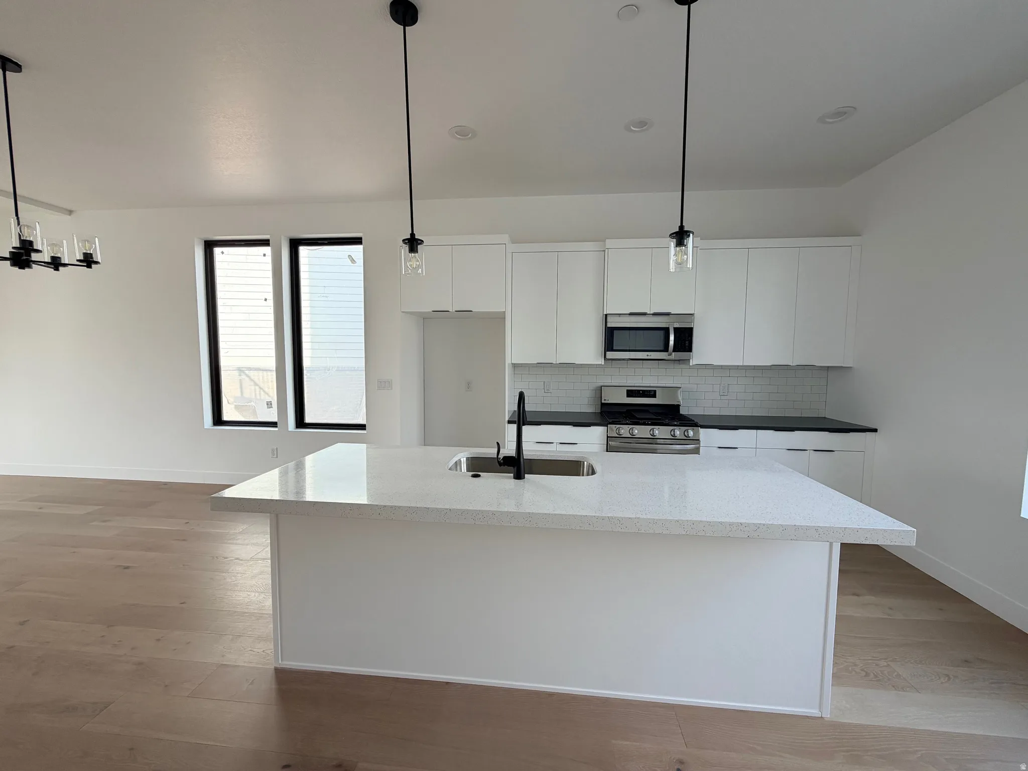 Kitchen featuring decorative light fixtures, stainless steel appliances, white cabinetry, light wood finished floors, and tasteful backsplash