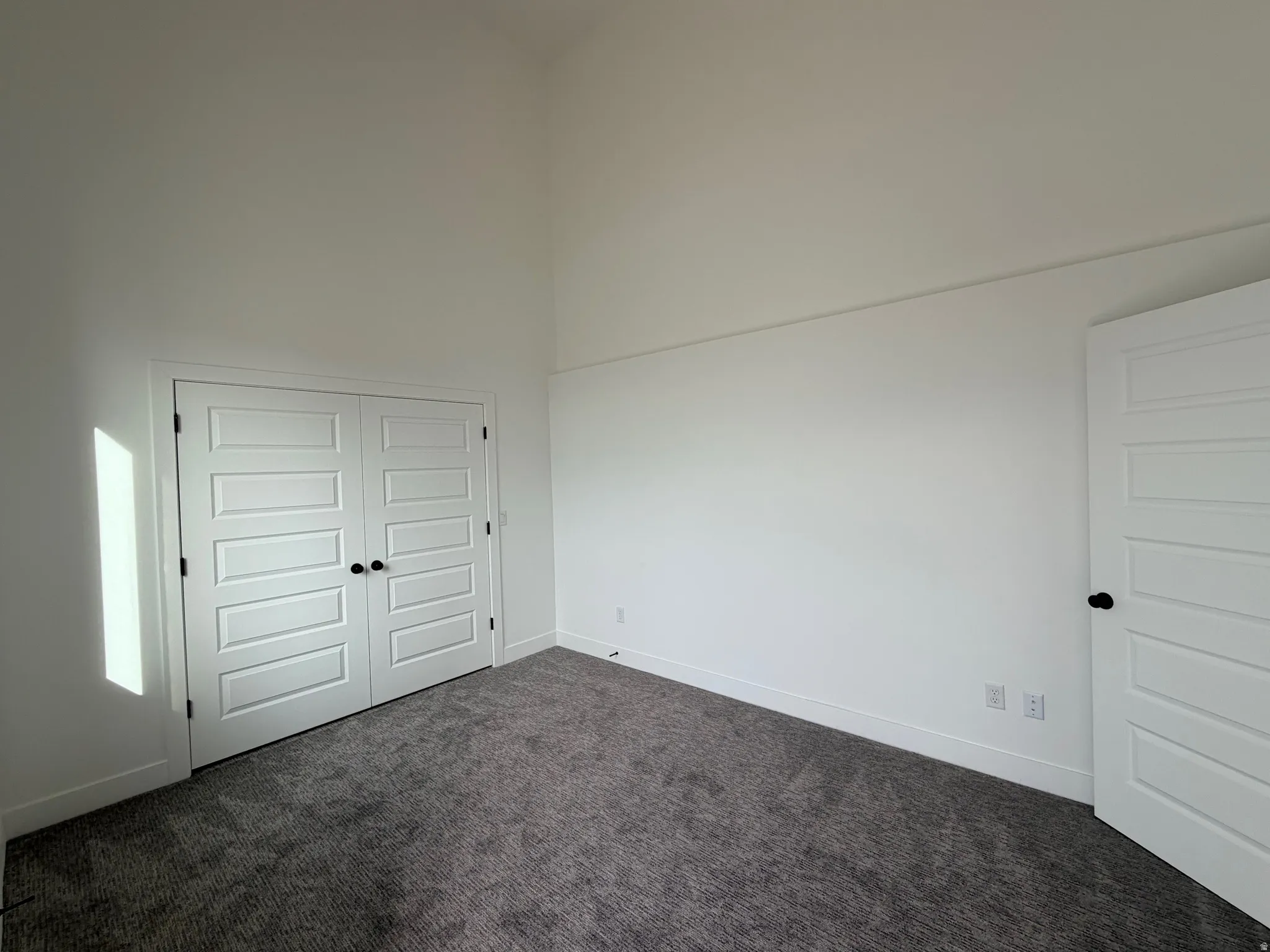 Unfurnished bedroom with a high ceiling, dark carpet, and a closet