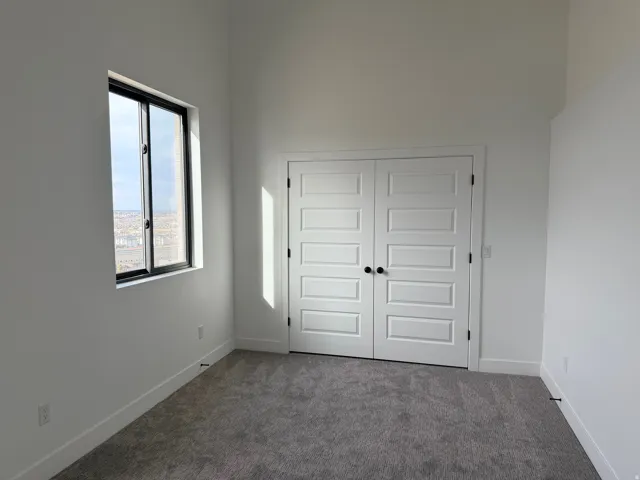 Unfurnished bedroom with dark carpet, a closet, and a high ceiling