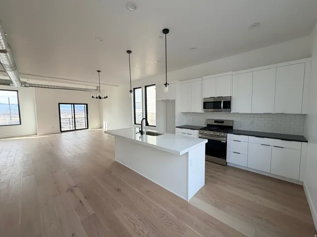 Kitchen featuring stainless steel appliances, white cabinets, tasteful backsplash, and hanging light fixtures
