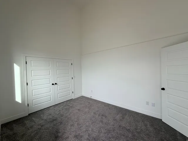 Unfurnished bedroom with a high ceiling, dark carpet, and a closet