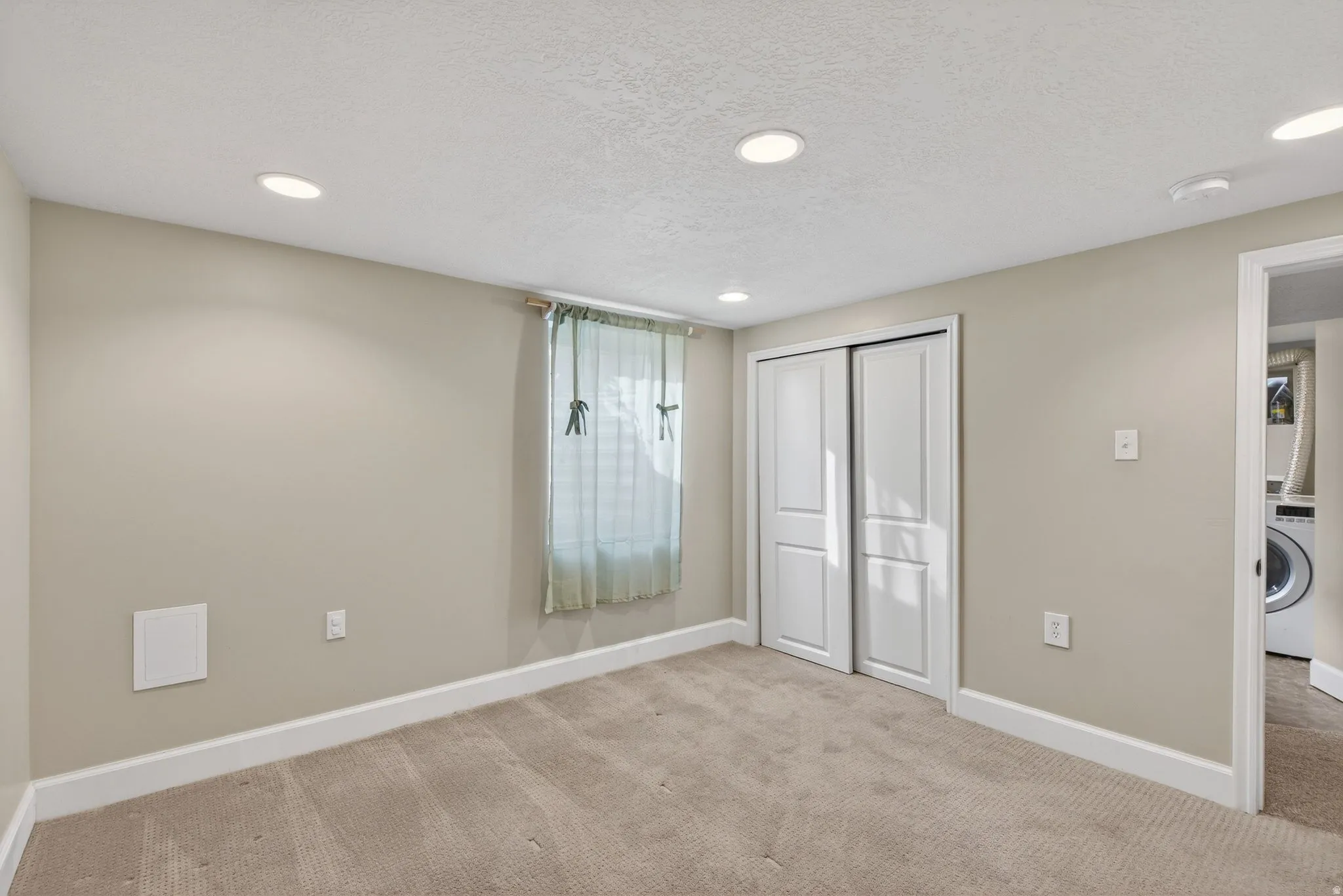 Unfurnished bedroom featuring a textured ceiling, light colored carpet, a closet, recessed lighting, and washer / clothes dryer
