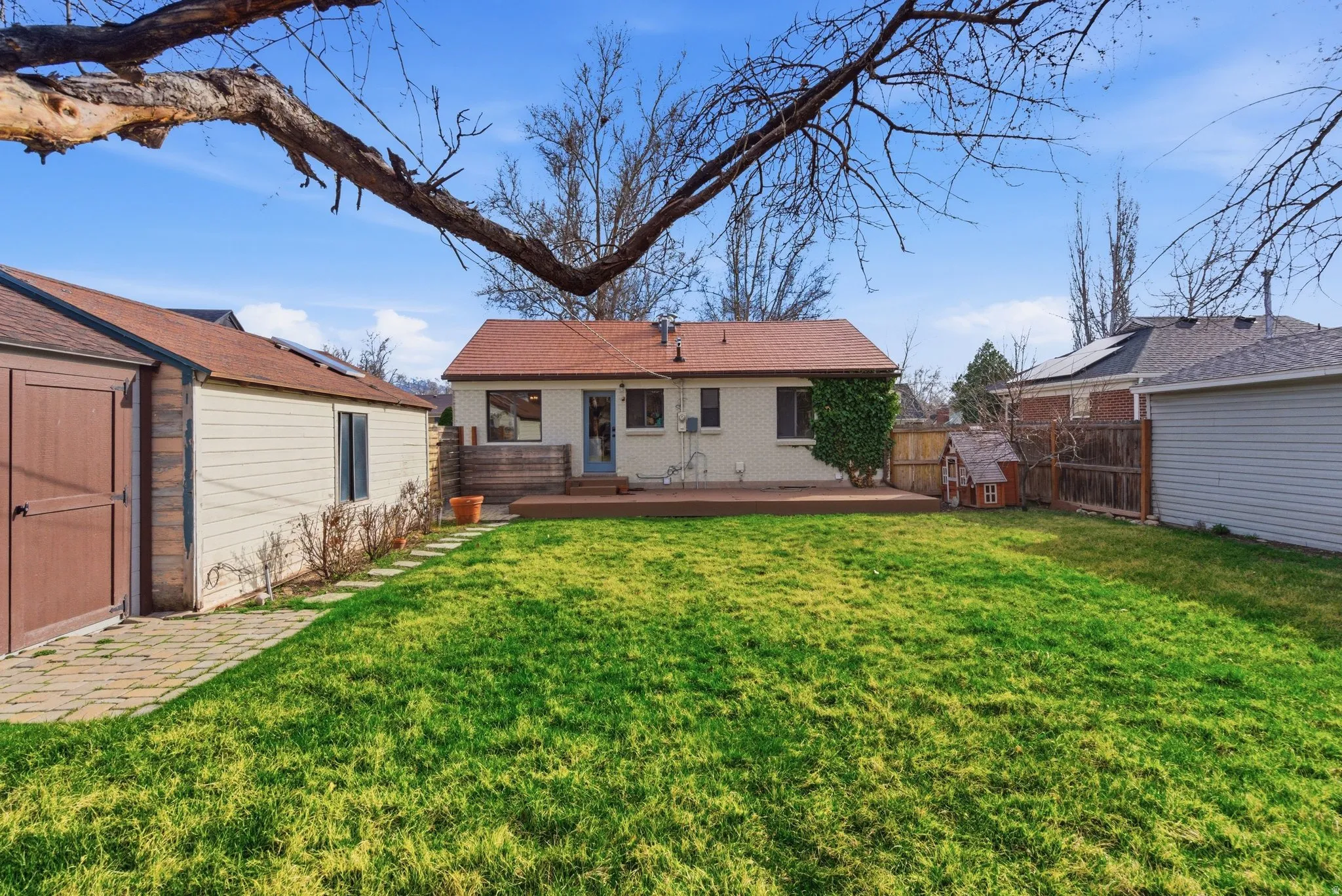 Rear view of property featuring brick siding, a fenced backyard, an outdoor structure, and a deck