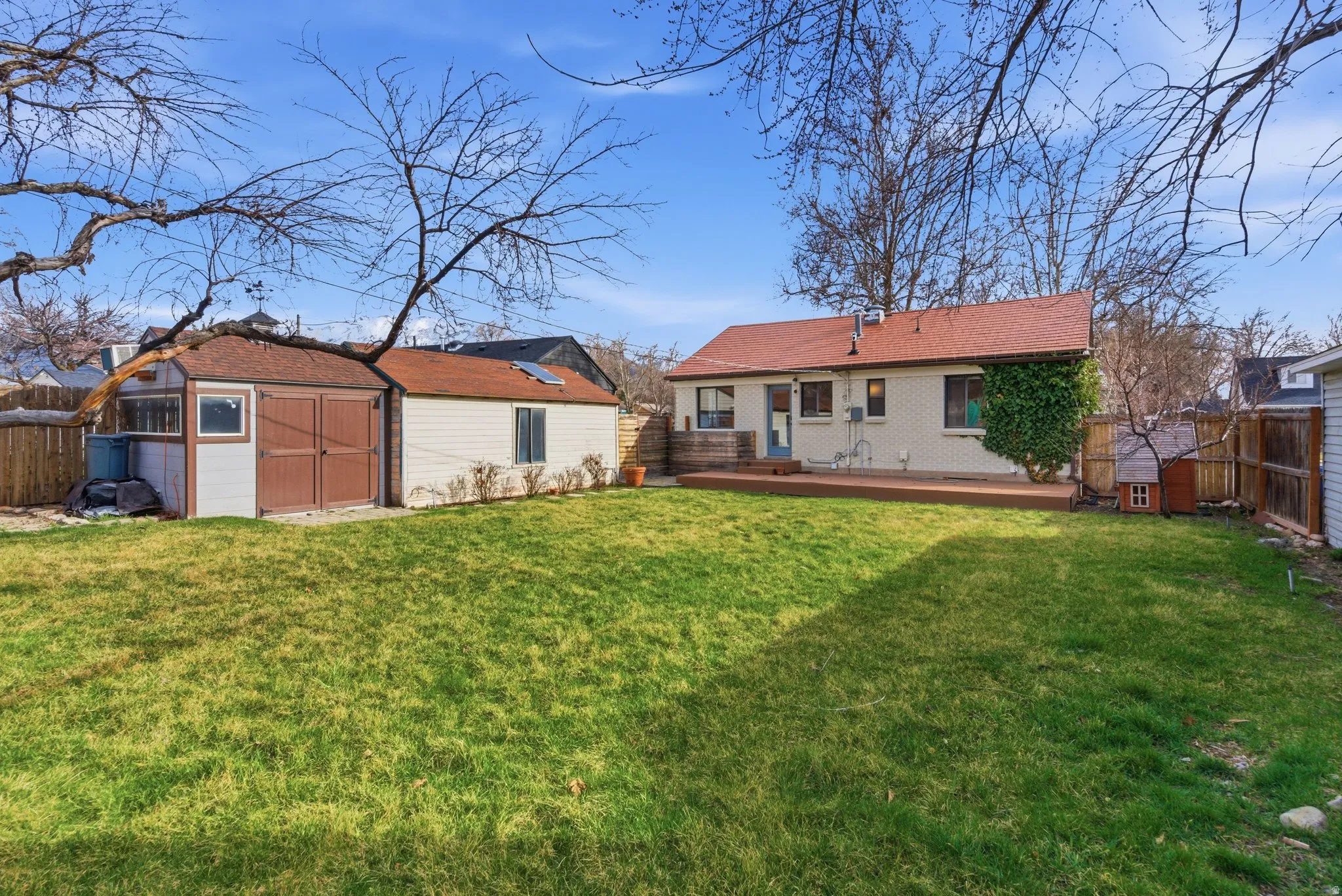 Rear view of property with a fenced backyard, a wooden deck, brick siding, and a storage unit
