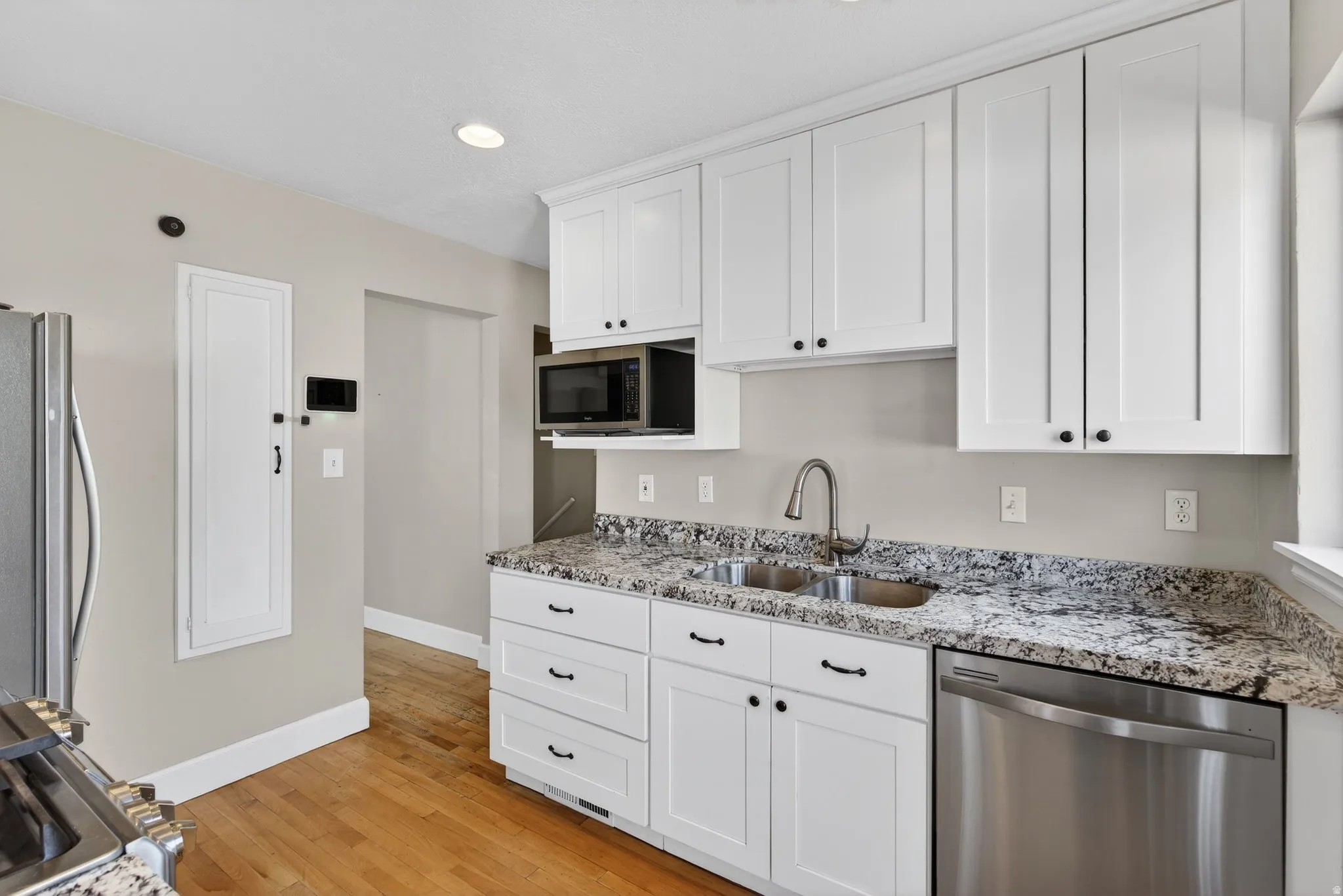 Kitchen featuring stainless steel appliances, white cabinetry, light stone countertops, light wood finished floors, and recessed lighting