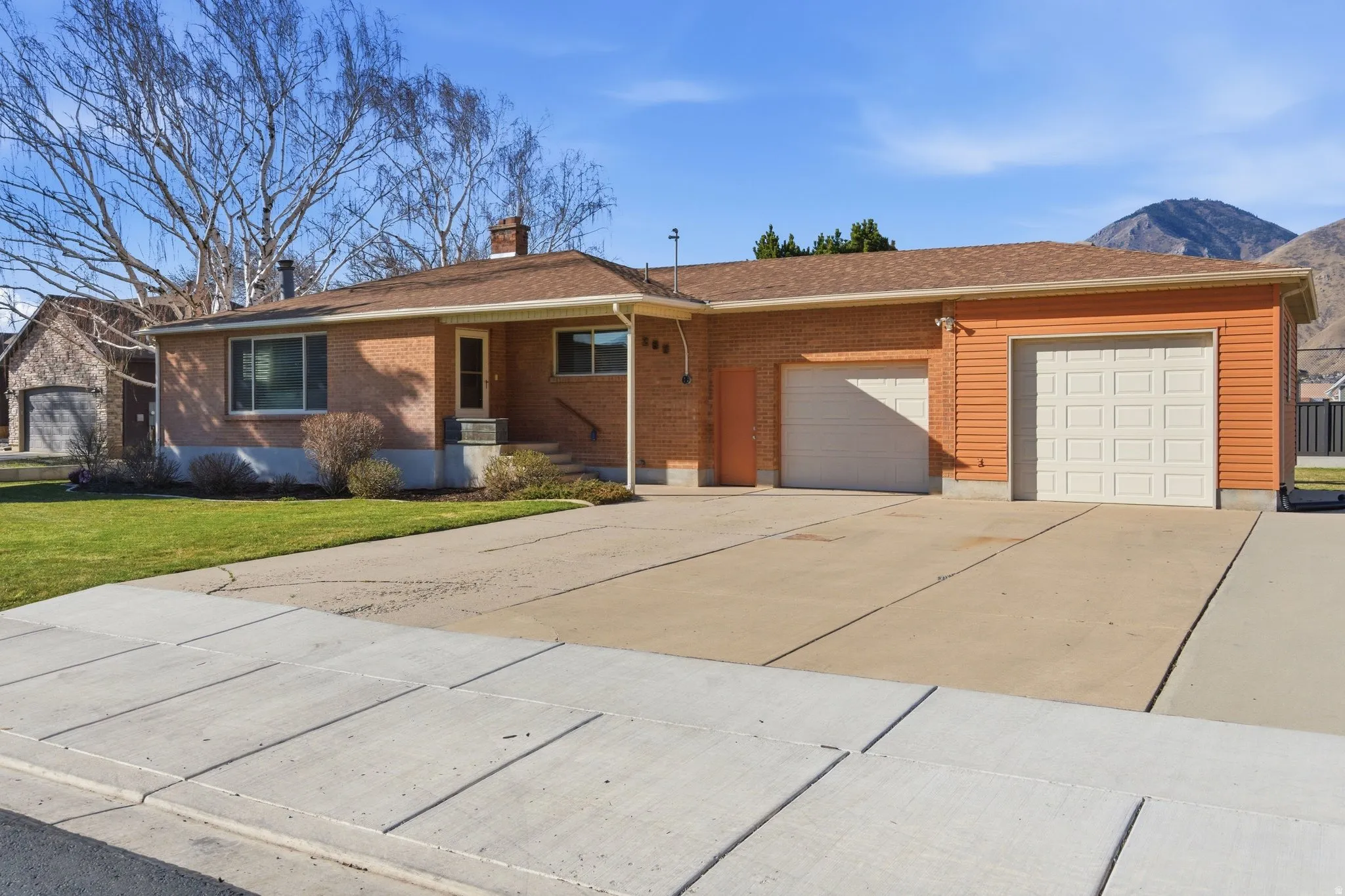 Single story home with a garage, brick siding, concrete driveway, a chimney, and a front lawn