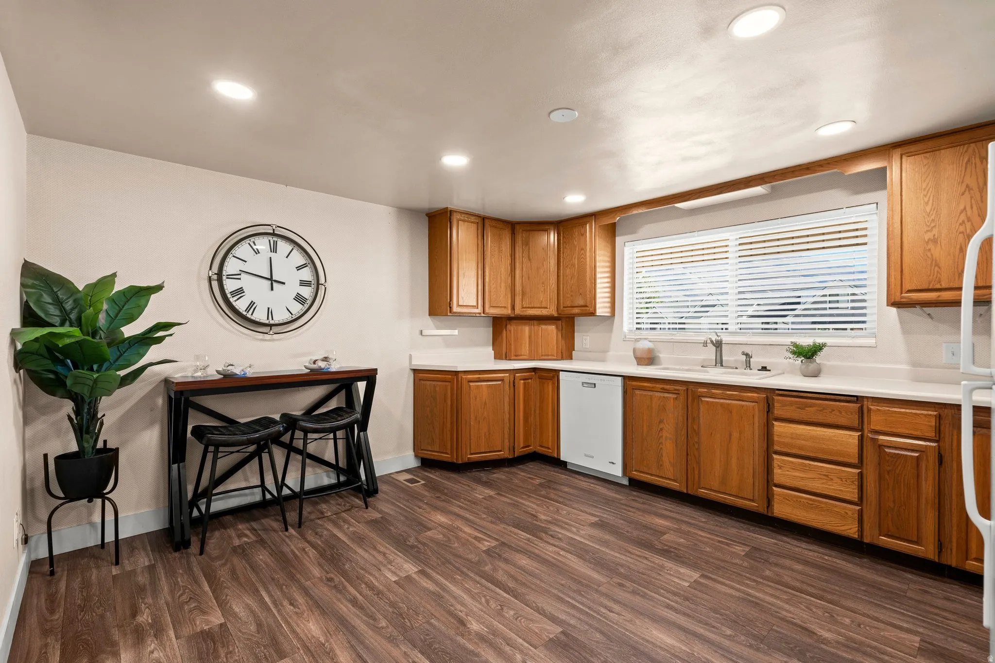 Kitchen featuring wood finish cabinetry, light countertops, white dishwasher, dark wood-type flooring, and recessed lighting