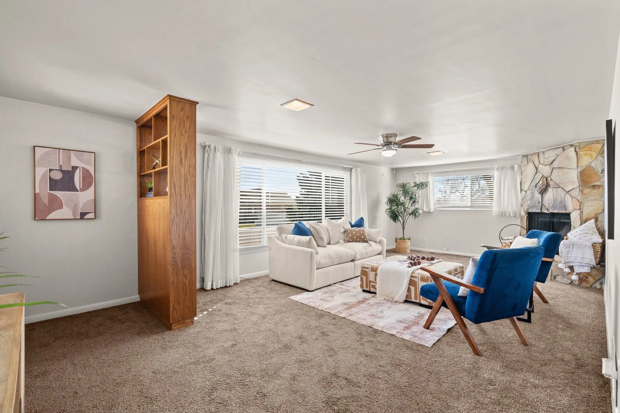 Living area with a ceiling fan, carpet, and a stone fireplace