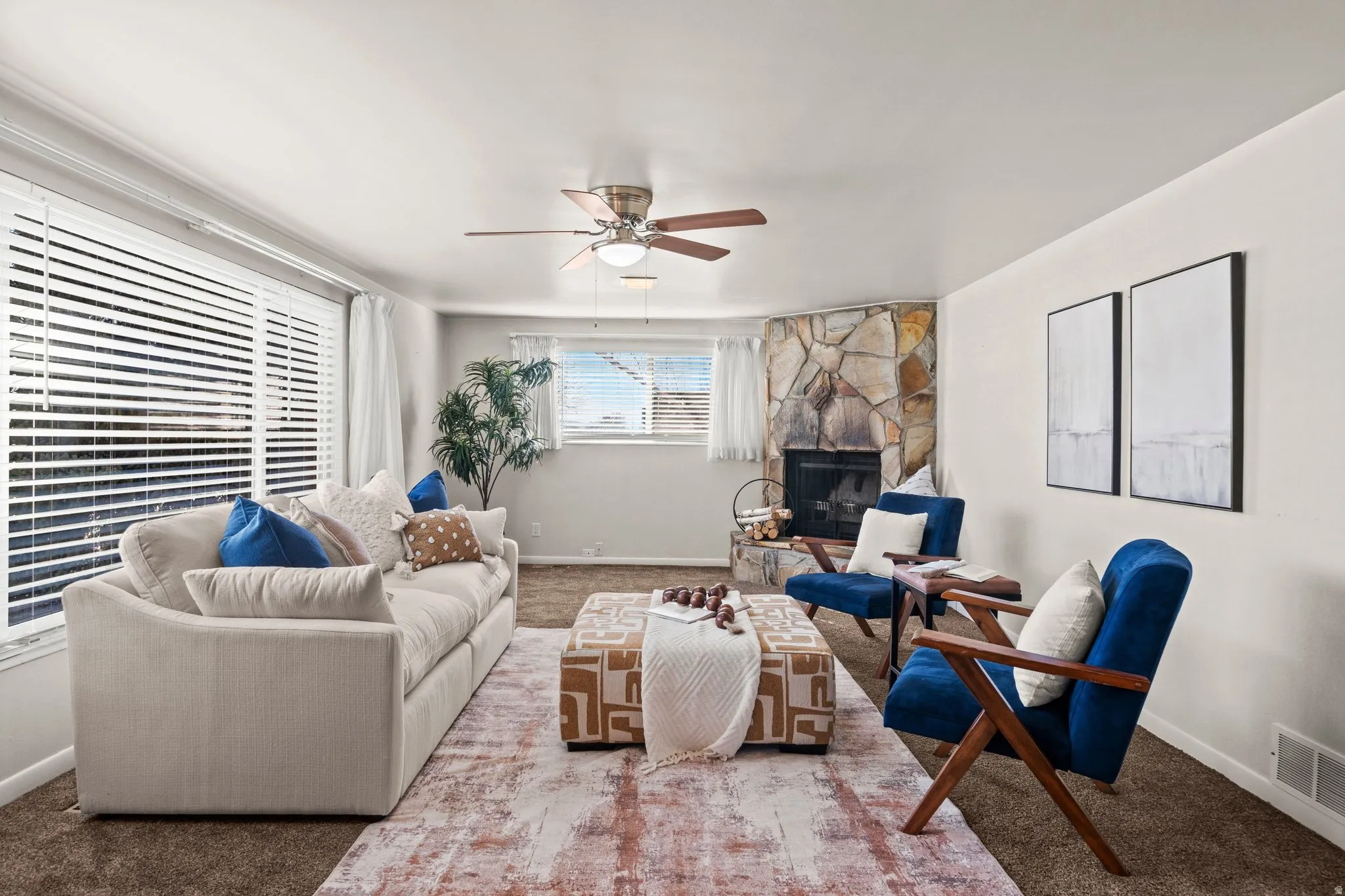 Living room with a ceiling fan, a stone fireplace, and carpet flooring