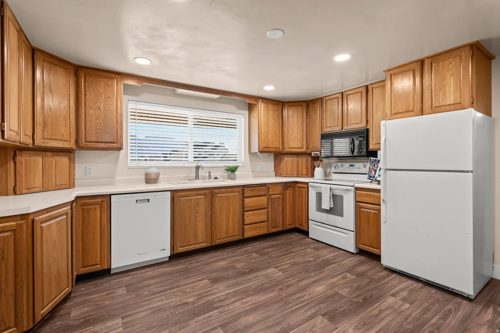 Kitchen with white appliances, light countertops, wood finish cabinetry, dark wood-style flooring, and recessed lighting