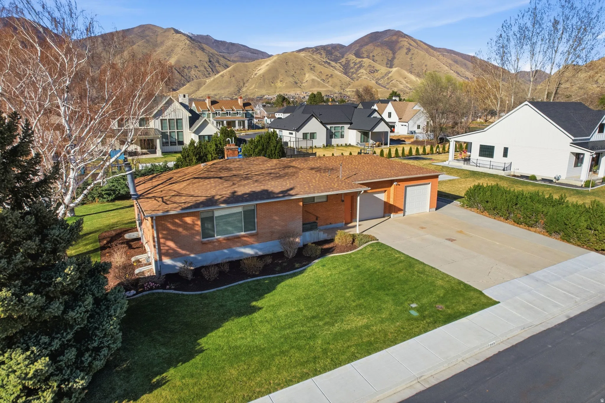 View of front facade with concrete driveway, brick siding, a mountain view, a front lawn, and a residential view