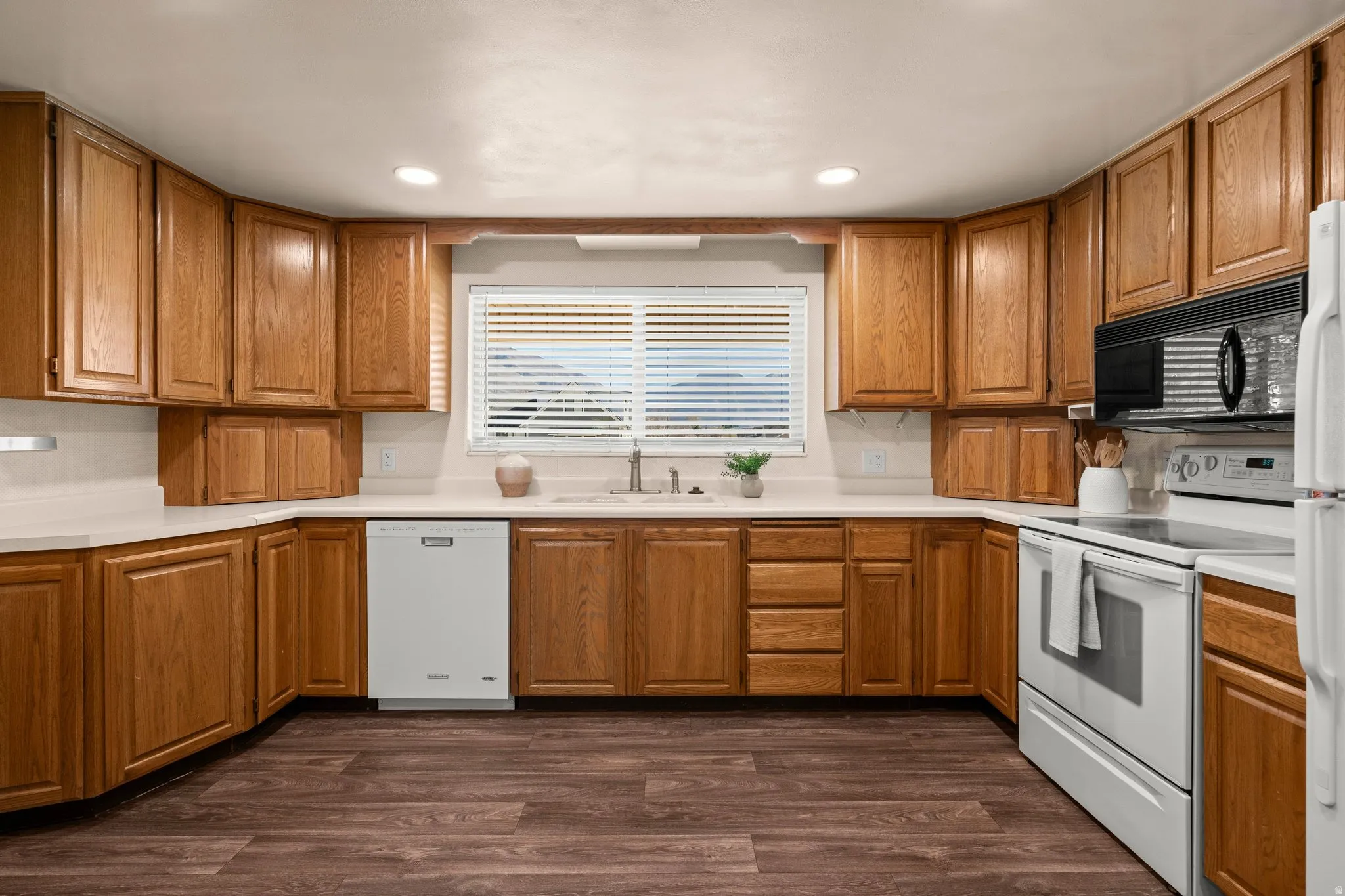 Kitchen featuring white appliances, light countertops, wood finish cabinets, dark wood-style flooring, and recessed lighting