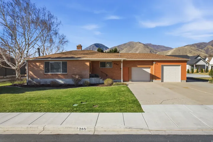 Ranch-style house featuring brick siding, driveway, an attached garage, a chimney, and a front yard