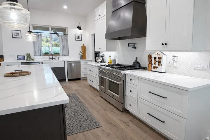 Kitchen featuring stainless steel appliances, light stone countertops, pendant lighting, light wood-style floors, and dual tone cabinets