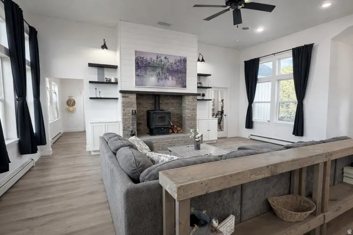 Living area with a wood stove, light wood finished floors, a ceiling fan, baseboard heating, and recessed lighting