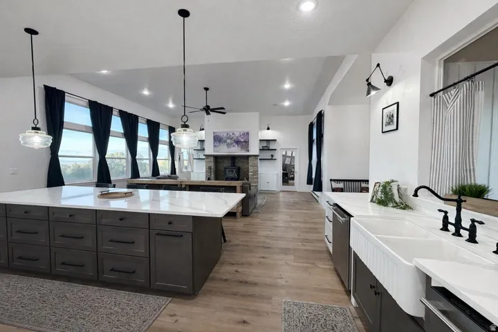 Kitchen featuring open floor plan, ceiling fan, light wood-style floors, light stone counters, and a fireplace