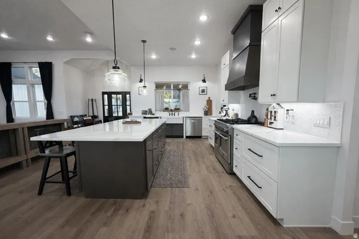 Dual tone kitchen with dual tone cabinetry, stainless steel appliances, light stone counters, a spacious island, and light wood finished floors