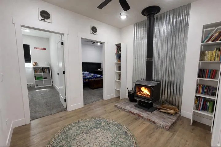 Living room featuring ceiling fan, a wood stove, and light wood finished floors