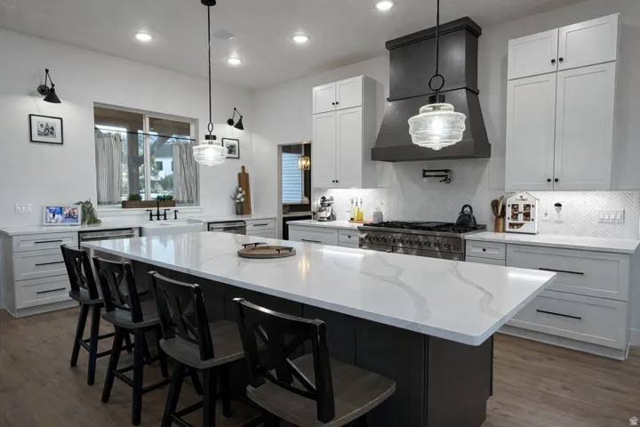Kitchen featuring two tone color scheme, a kitchen breakfast bar, double oven range, light stone counters, and dark wood-style floors