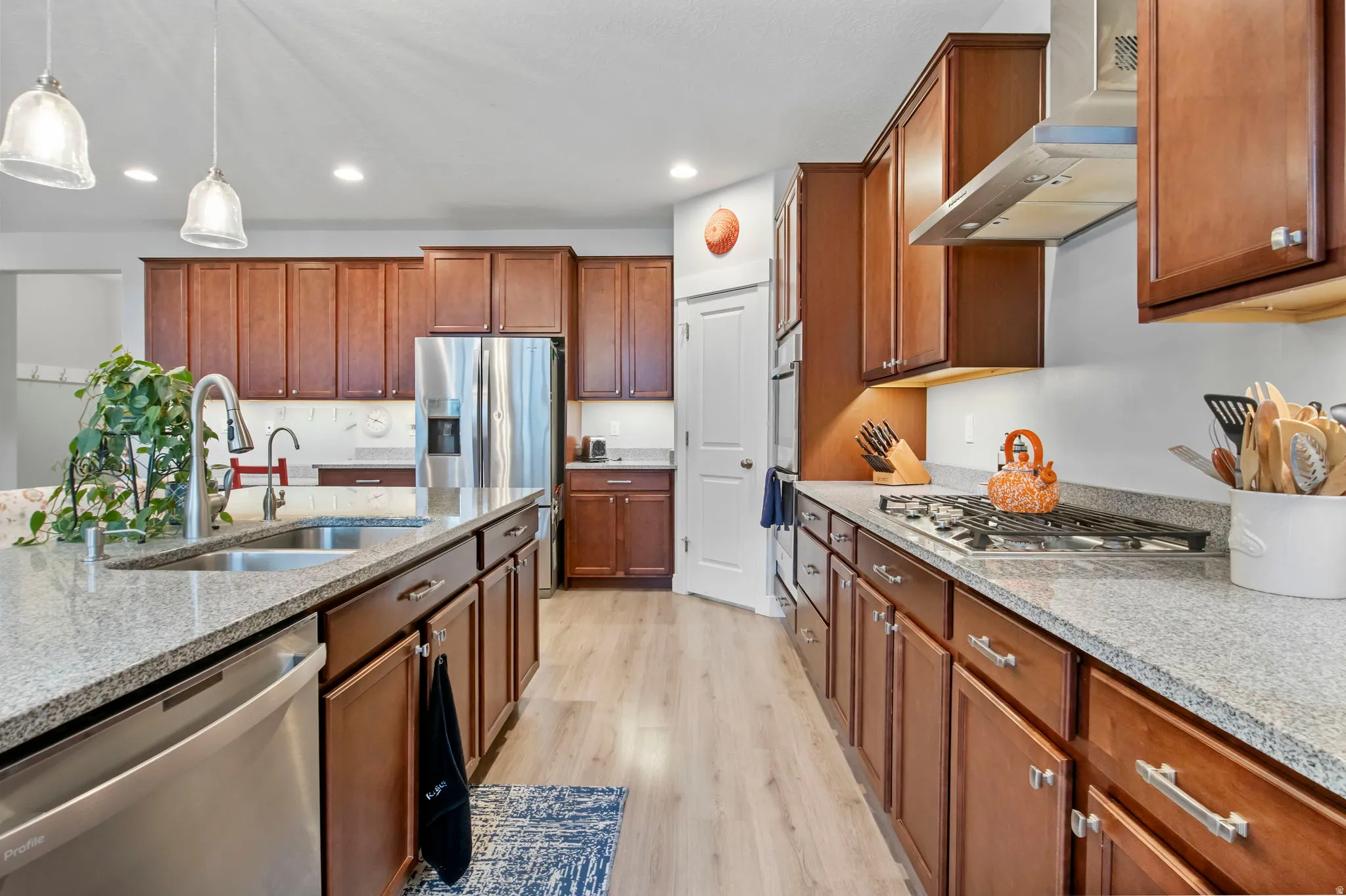 Kitchen featuring light stone countertops, stainless steel appliances, light wood-style floors, and pendant lighting
