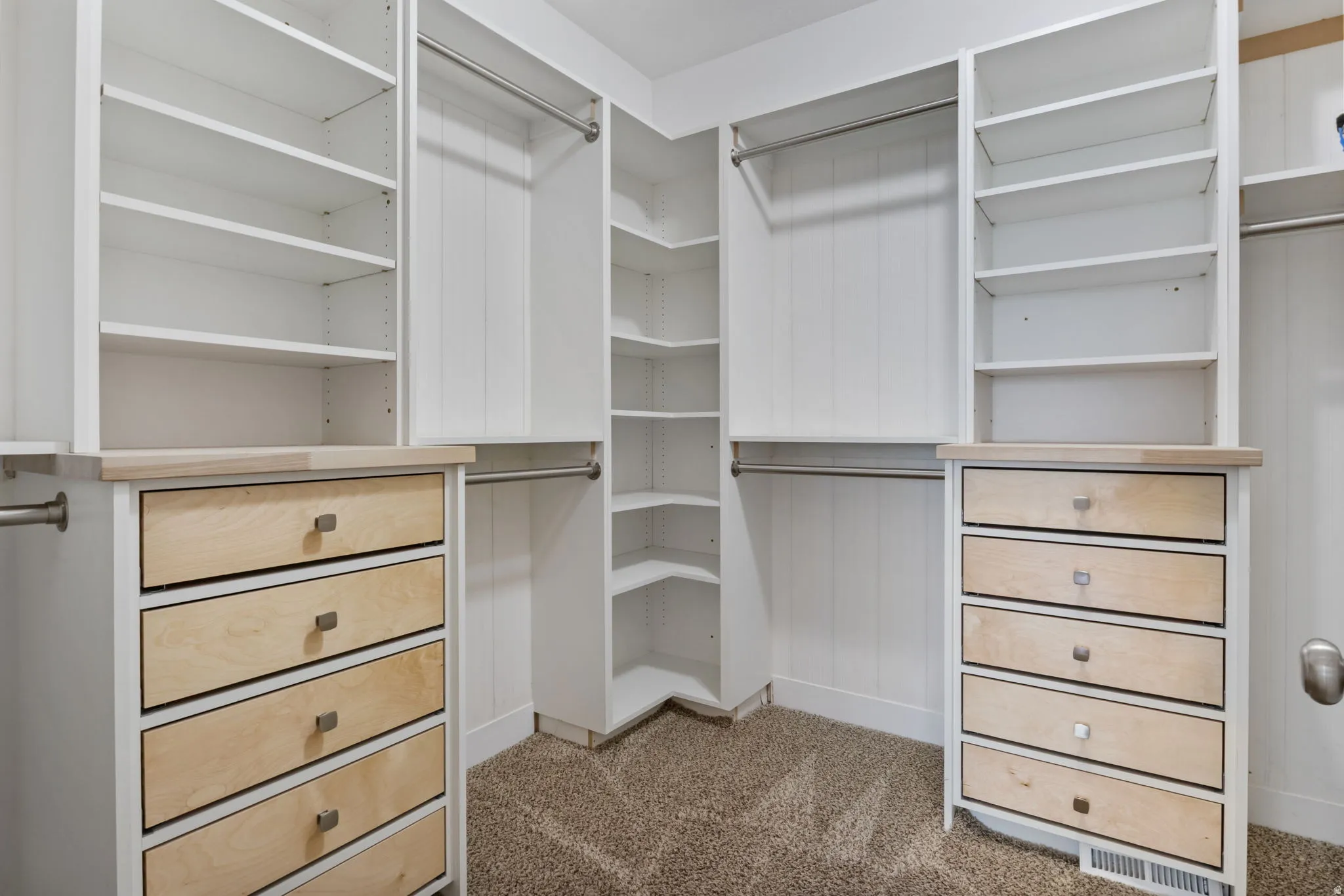 Custom closet system featuring white cabinetry, light wood-finish drawer fronts, and hardware