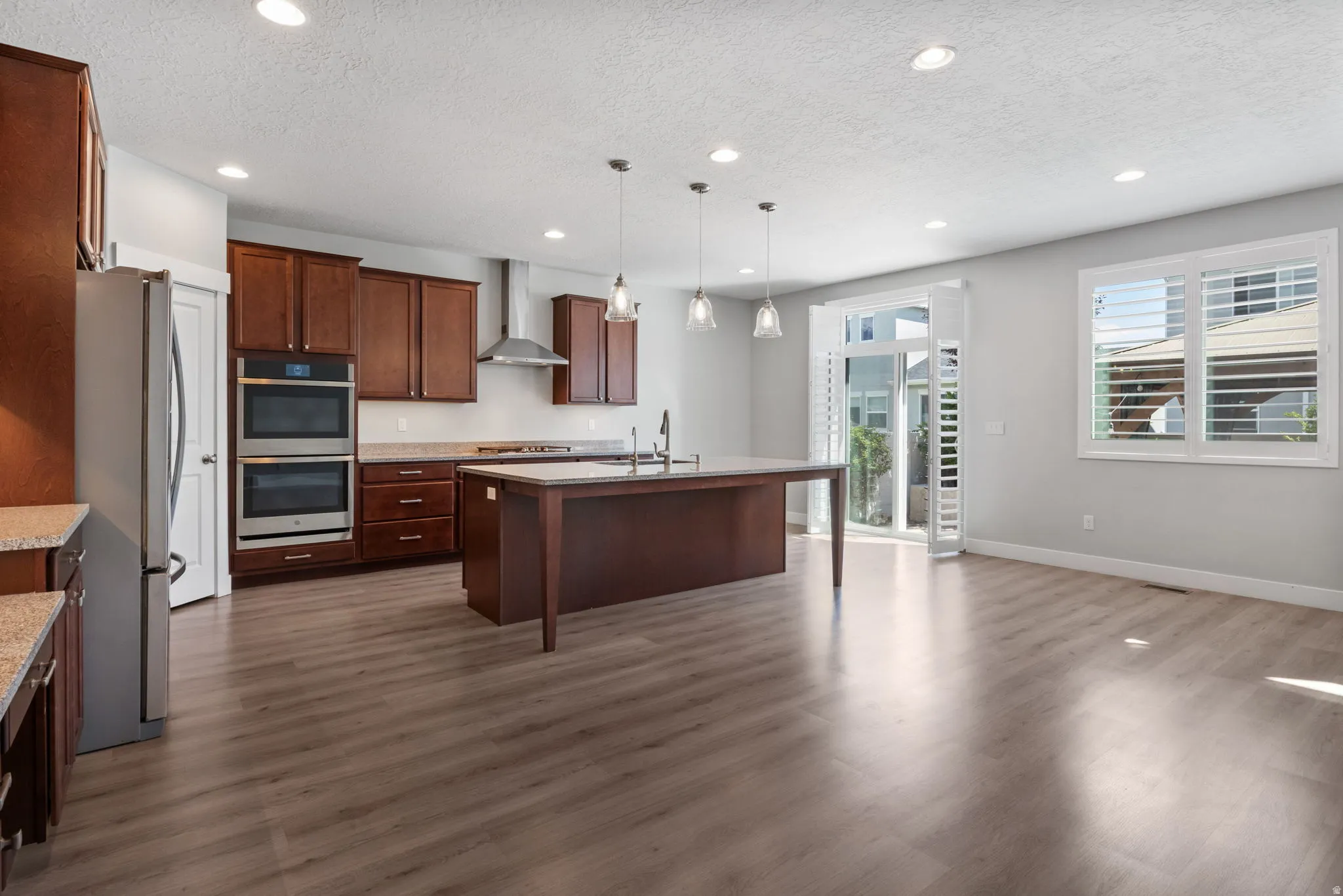 Open-concept kitchen and living area featuring wood-finish flooring, recessed lighting, and a large central island with pendant lighting