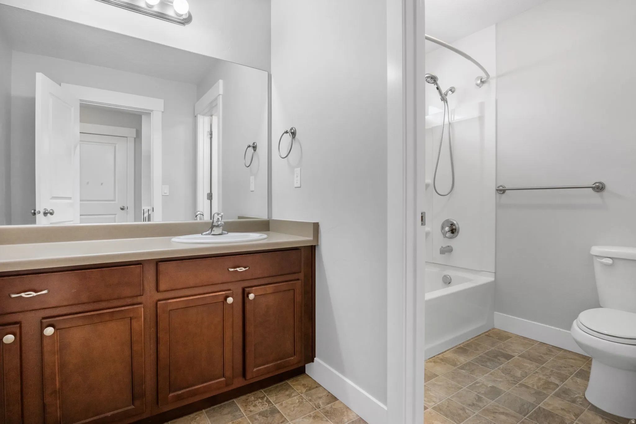Full bathroom featuring a single vanity with wood cabinetry, a large wall-mounted mirror, and a combination shower/tub with a curved shower rod