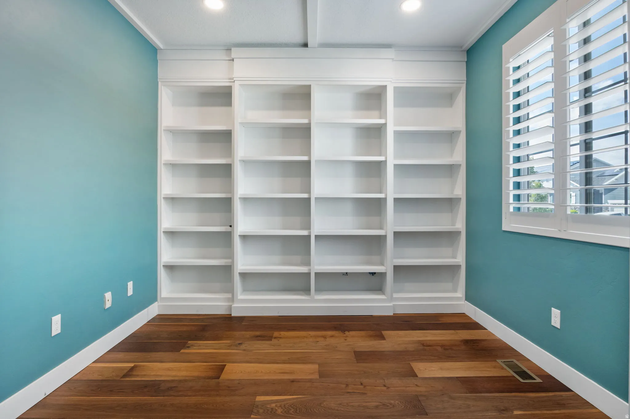 Built-in shelving units with adjustable shelves, wood-finish flooring, plantation shutters, recessed lighting.
