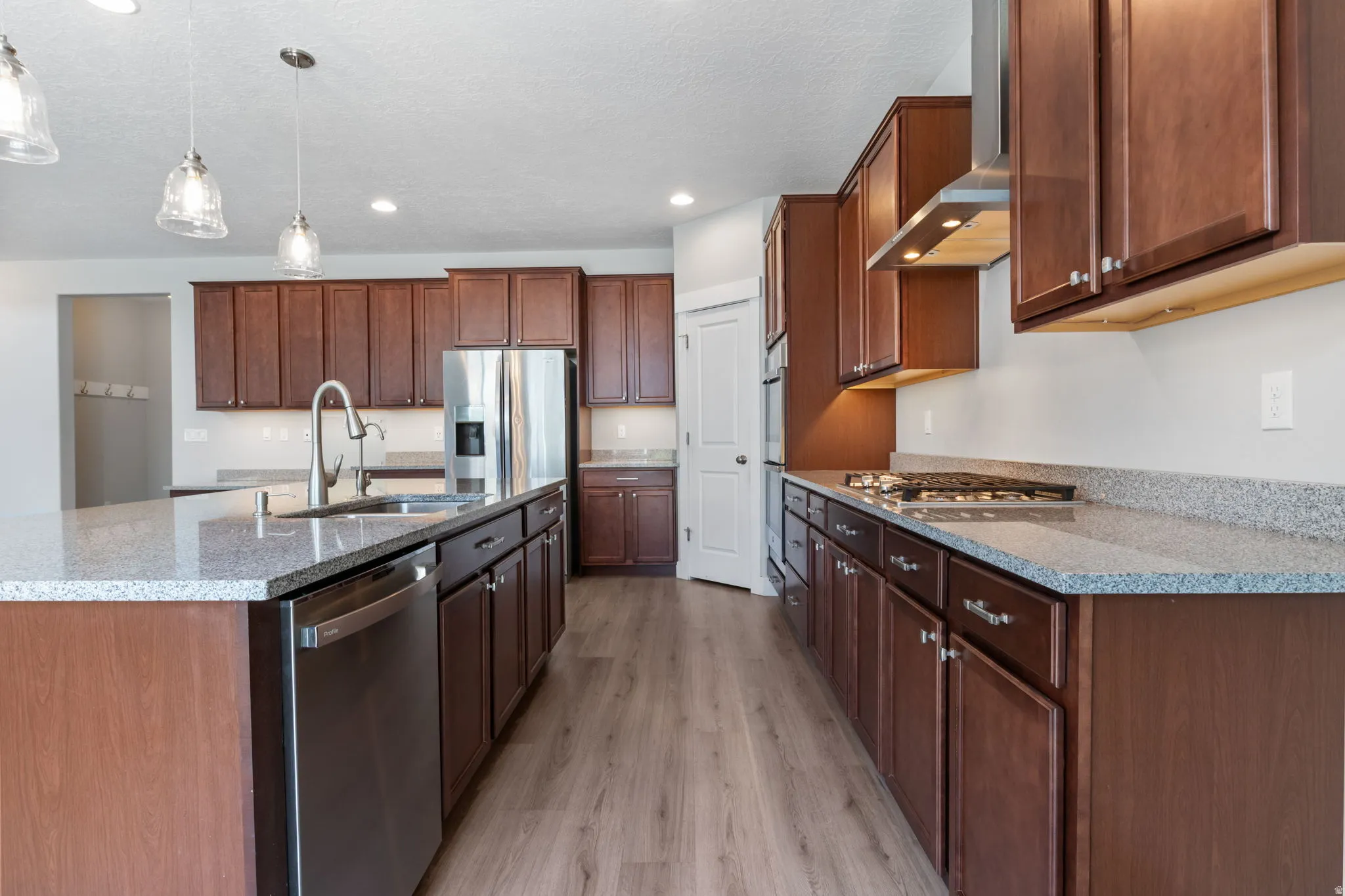 Kitchen featuring an oversized island with pendant lighting, stainless steel appliances, abundant cabinetry, stone-finish countertops, and wood-finish flooring