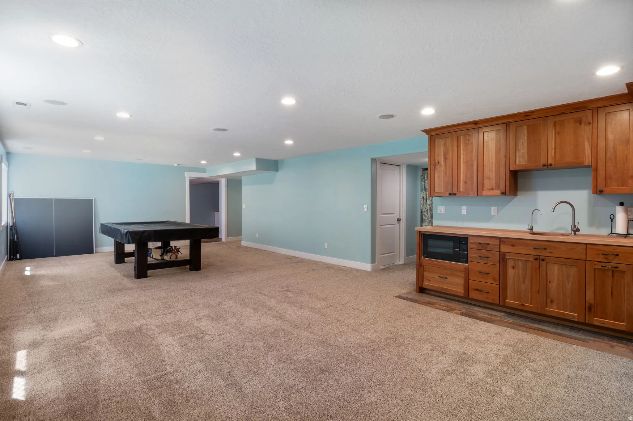 Open recreational room featuring a kitchenette with wood cabinetry, fridge and microwave.