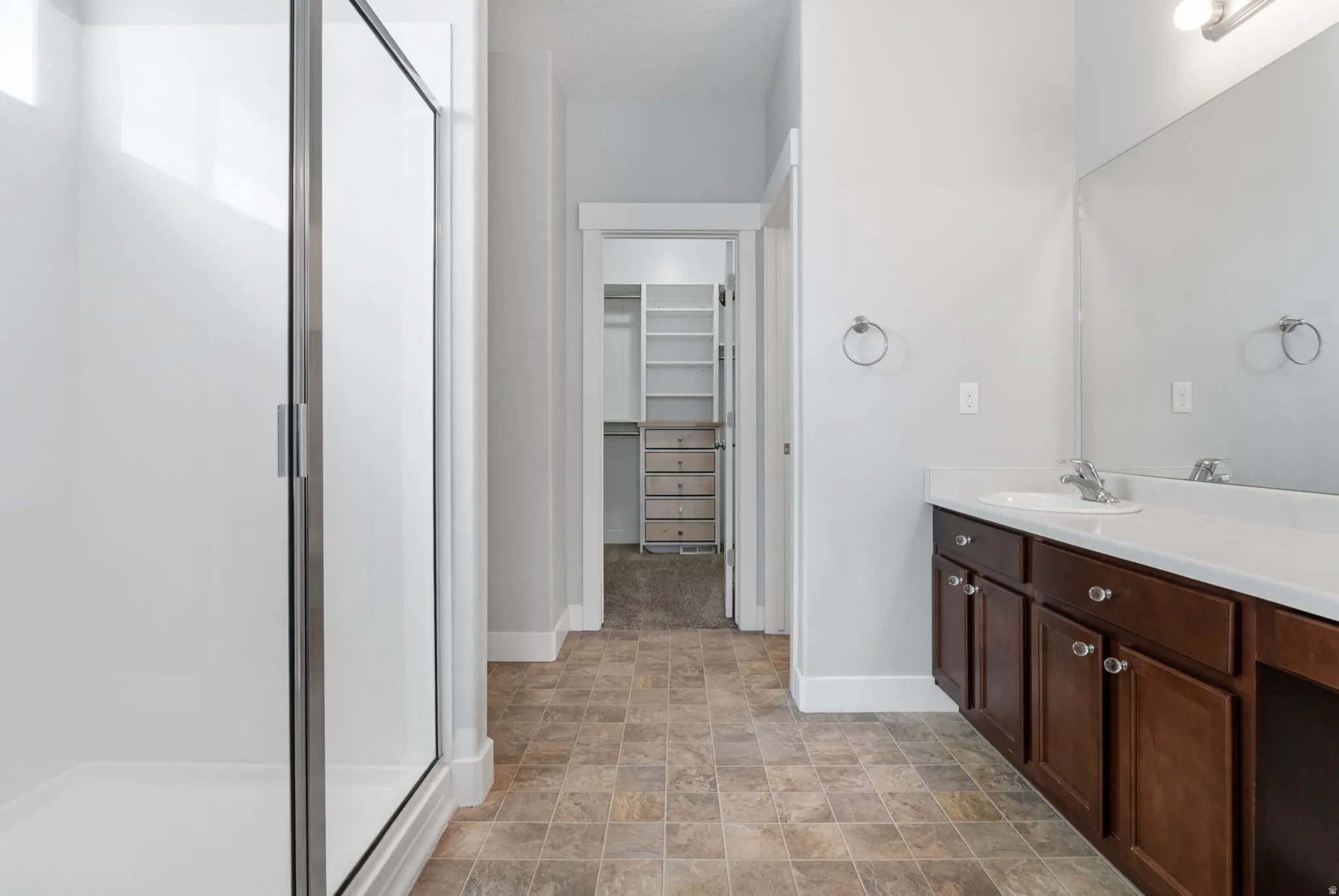 En Suite bathroom featuring a glass-enclosed shower, a single vanity with dark wood cabinetry, a white countertop, and a large wall mirror